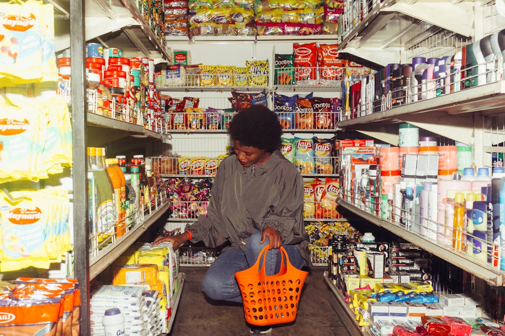 African American woman selecting products in a convenience store with an orange basket.