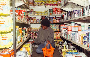 African American woman selecting products in a convenience store with an orange basket.