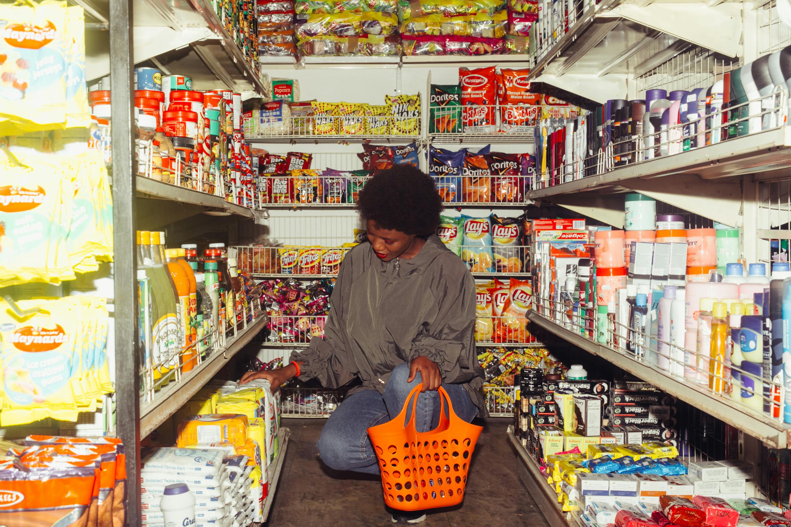 African American woman selecting products in a convenience store with an orange basket.